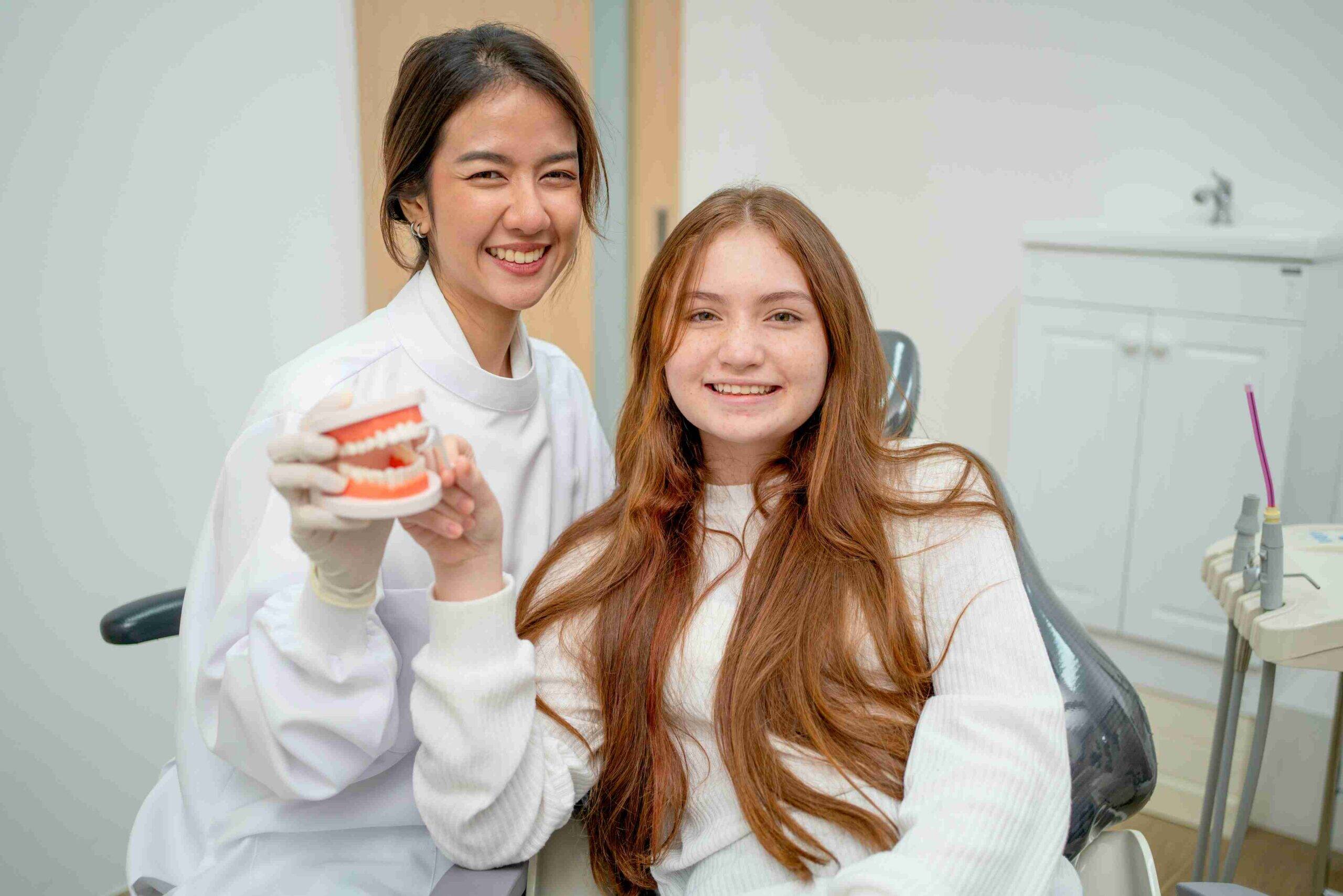 Smiling dentist and young patient holding a dental model.